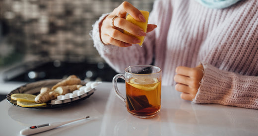 Mãos femininas espremendo limão fresco sobre uma chávena de chá quente, um remédio natural e caseiro para aliviar sintomas de gripe e constipação. Dicas de saúde no inverno.